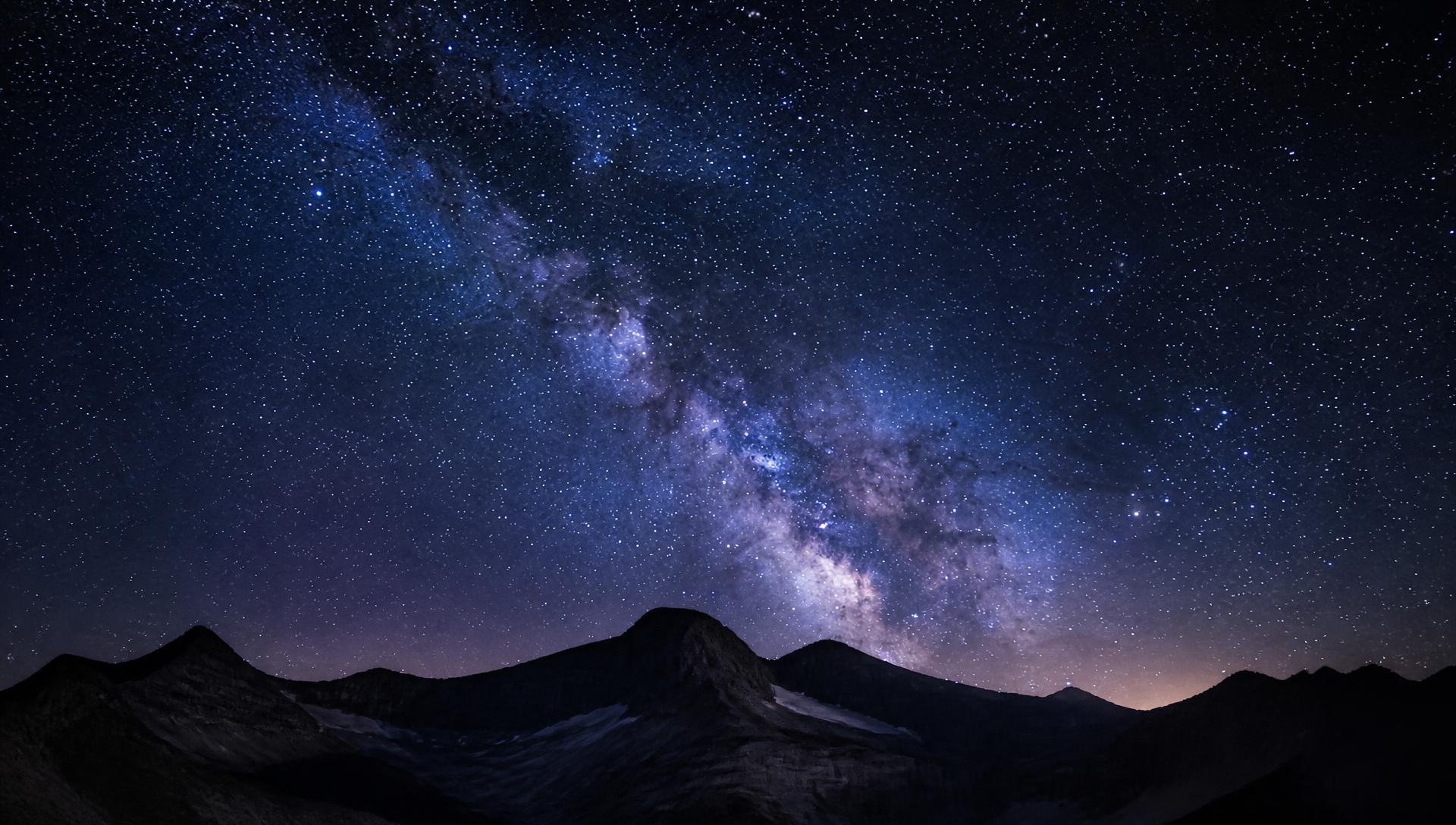 Deep-space starry night sky with a mountain silhouette along the horizon